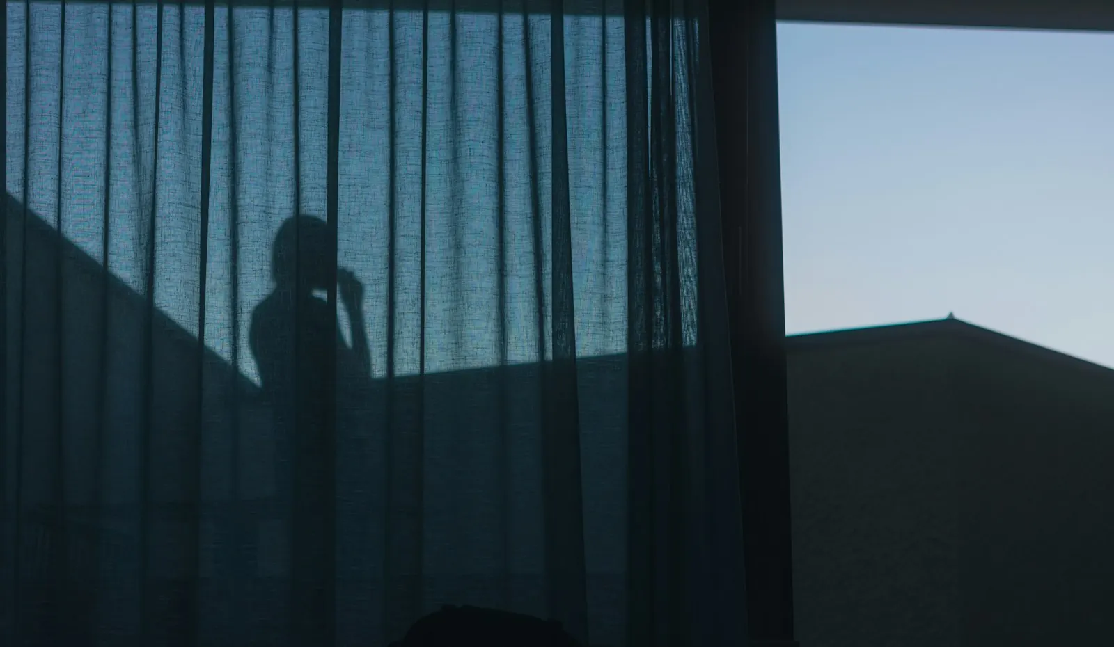 Silhueta de uma pessoa ao telemóvel atrás de um cortinado, em contraluz