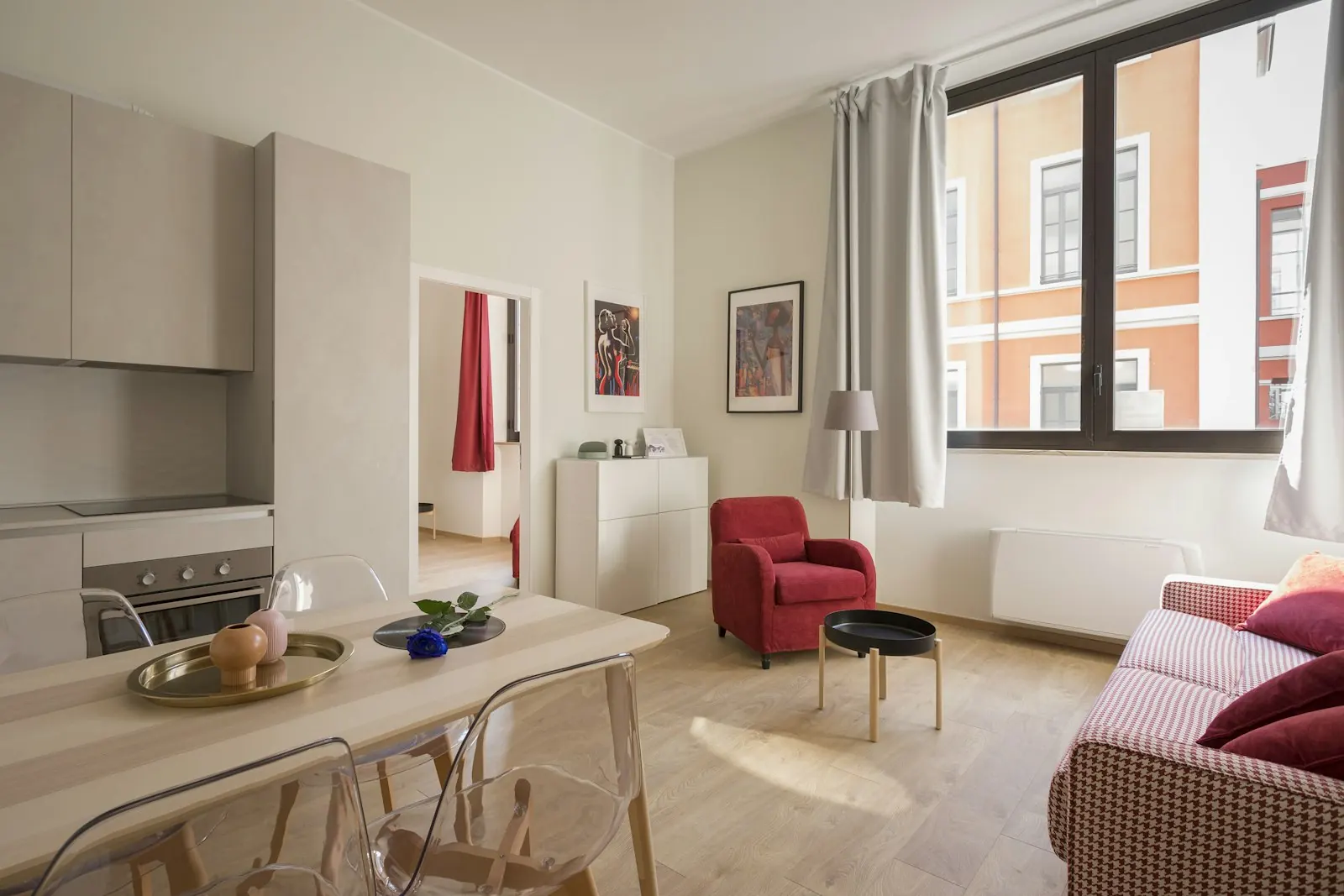Sala e cozinha de um apartamento com mesa de madeira, cadeira vermelha e luz de janela